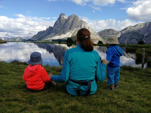 a woman and two children sitting on the grass near a lake at Canalhof in Antermoia