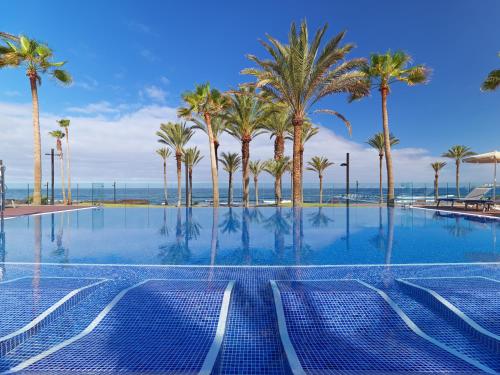 a swimming pool with palm trees and the ocean at H10 Conquistador in Playa de las Americas