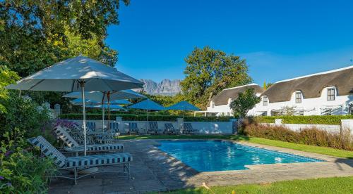 einem Pool mit Stühlen und einem Sonnenschirm neben einem Haus in der Unterkunft Erinvale Estate Hotel & Spa in Somerset West