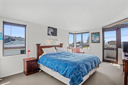 a bedroom with a bed with a blue comforter and windows at Kiwiana Bach - Waihi Beach Holiday Home in Waihi Beach