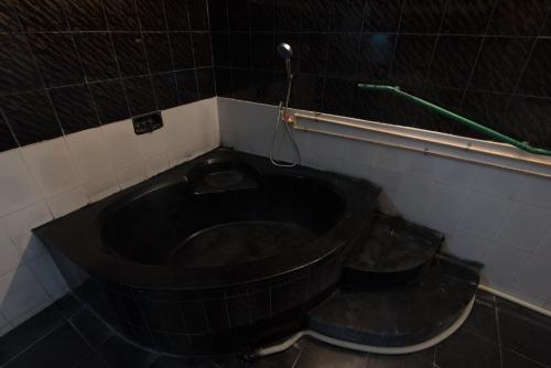 a black bath tub in a bathroom with two buckets at Arunik Inn in Puducherry
