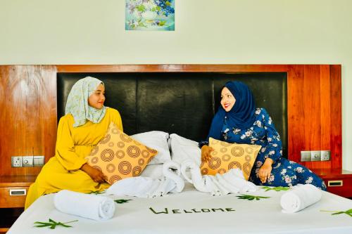 two women sitting on a bed with pillows at La Cabana, Maamigili in Maamigili