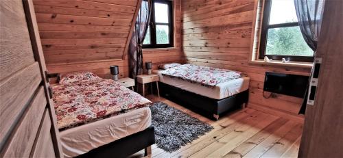 two beds in a room with wooden walls and windows at Ostoja Krasne in Uścimów