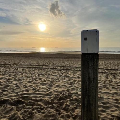 a wooden post on a beach with the sun setting at Beach House For You - Luxe verblijf, 5 min van het strand in Katwijk aan Zee