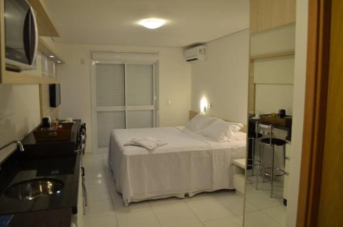 a bedroom with a white bed and a kitchen at Executive 206 Sem Garagem in Caxias do Sul