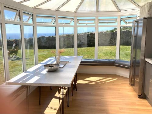 a dining room with a table in a conservatory at Lovely spacious flat with sea views, sunsets, garden and woodburner in Sennen