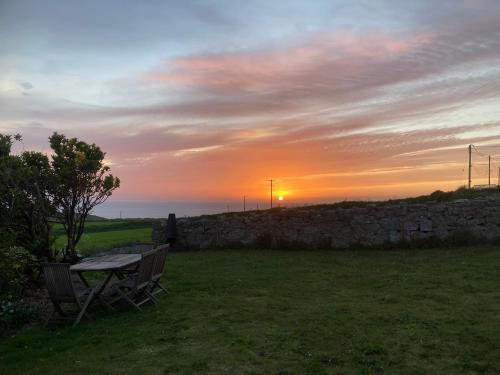 a table and chairs in a field with a sunset at Lovely spacious flat with sea views, sunsets, garden and woodburner in Sennen