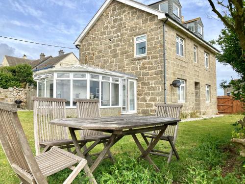 a wooden table and chairs in front of a house at Lovely spacious flat with sea views, sunsets, garden and woodburner in Sennen