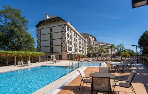 ein Hotelpool mit Tischen und Stühlen und ein Gebäude in der Unterkunft Blue Flat Pedra Azul - Com Vista pra Pedra in Pedra Azul