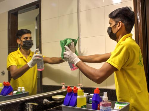 a man wearing a mask and gloves cleaning a mirror at Lime Stays B&B GK-2 at Greater Kailash Metro South Delhi nearby Saket Select City in New Delhi