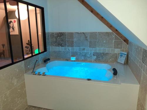 La salle de bains est pourvue d'une baignoire bleue et d'une fenêtre. dans l'établissement Appartement chaleureux avec Jacuzzi, à Banassac
