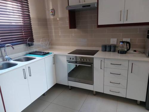 a kitchen with white cabinets and a sink and a stove at 2-bedroom apartment in a security complex in Kimberley