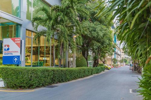 a street in front of a building with palm trees at Amp Am House Bangkok Hotel in Bangkok