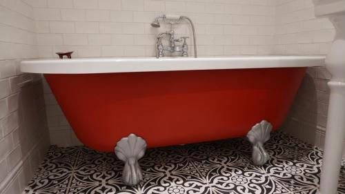a red bath tub in a bathroom with a tile floor at Shabby Chic - apartment in the Heart of Vilnius Old Town in Vilnius