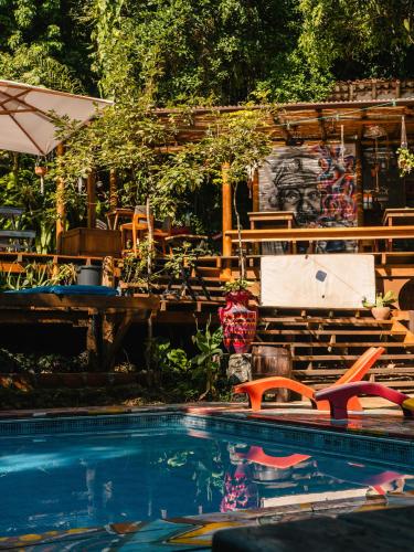 a swimming pool with chairs and a house in the background at Hostel Da Vila Ilhabela in Ilhabela