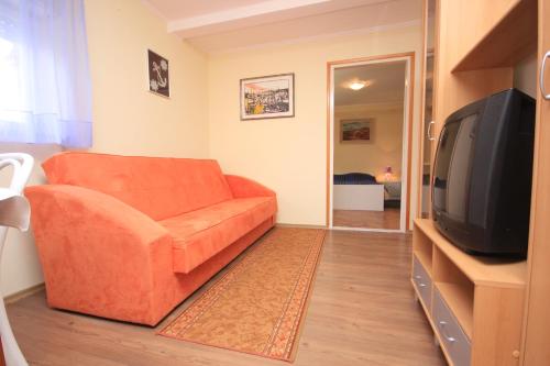 ein Wohnzimmer mit einem orangenen Sofa und einem TV in der Unterkunft Apartments and rooms by the sea Medveja, Opatija - 2305 in Lovran
