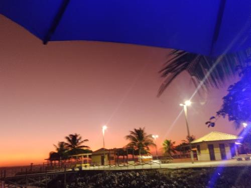 a blue umbrella and some buildings and palm trees at night at Pousada dos Corais in Mundaú
