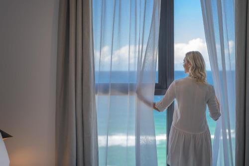a woman looking out the window of a hotel room at Meriton Suites Surfers Paradise in Gold Coast