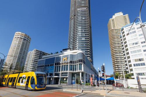 a yellow train in front of a building with tall buildings at Meriton Suites Surfers Paradise in Gold Coast