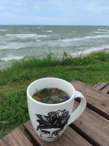 uma chávena de café sentada numa mesa perto do oceano em Vilnīši em Ulmale