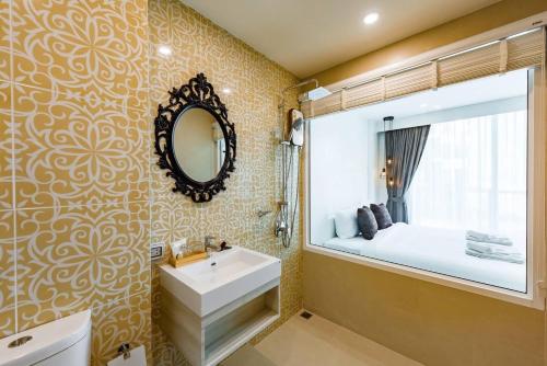 ein Bad mit einem Waschbecken, einem Spiegel und einem Bett in der Unterkunft LullaBella Hotel in Patong Beach