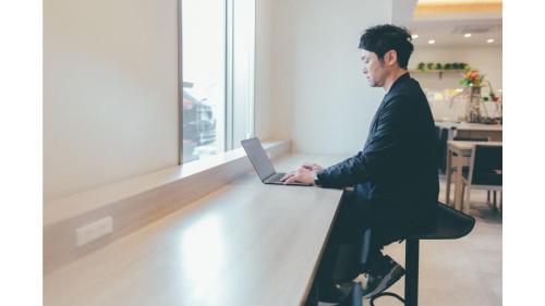 Kuretake Inn Premium Shizuoka Annex في شيزوكا: رجل يجلس على طاولة مع جهاز كمبيوتر محمول