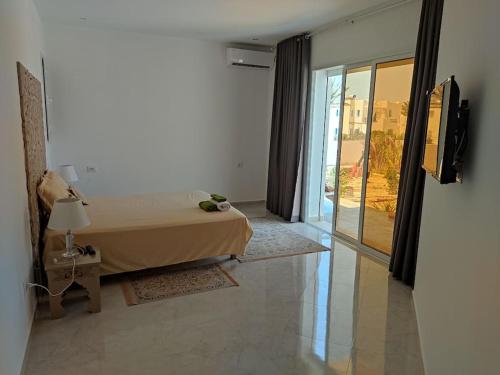 a bedroom with a bed and a large window at VILL LA REINE JERBA avec piscine in Djerba