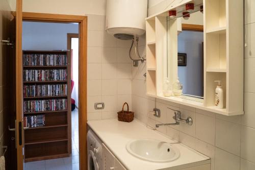 La salle de bains est pourvue d'un lavabo et d'une étagère avec des DVD. dans l'établissement Elegant apartment in residence with pool, à Acireale