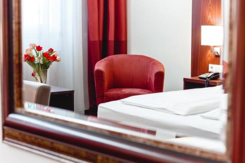 a bedroom with a bed and a red chair and a mirror at Hotel Allegro Wien in Vienna