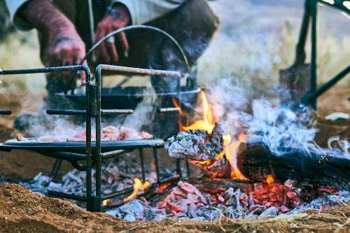 eine Person, die Essen über einem Lagerfeuer kocht in der Unterkunft We Kebi Safari Lodge in Sesriem