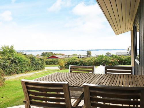 6 person holiday home in Ebberup في Helnæs By: طاولة وكراسي خشبية على شرفة مطلة على المحيط