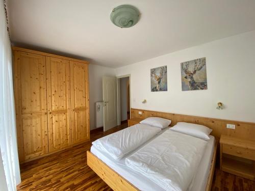 - une chambre avec un lit doté de draps blancs et de placards en bois dans l'établissement Amalia Apartment, à Santa Cristina Valgardena