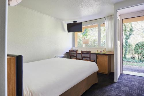 a bedroom with a bed and a desk and a window at Kyriad Caen Nord - Hérouville-Saint-Clair in Hérouville-Saint-Clair