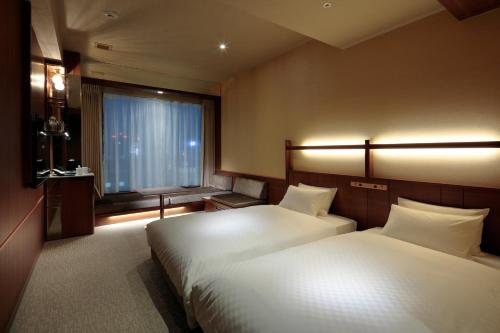 a hotel room with two beds and a window at Candeo Hotels Kumamoto Shinshigai in Kumamoto