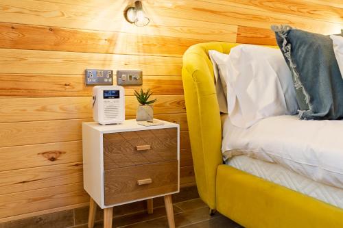 a bedroom with a yellow bed and a nightstand with a alarm clock at Cliff Stud Retreat - Luxury lodges and cosy cottages in Helmsley