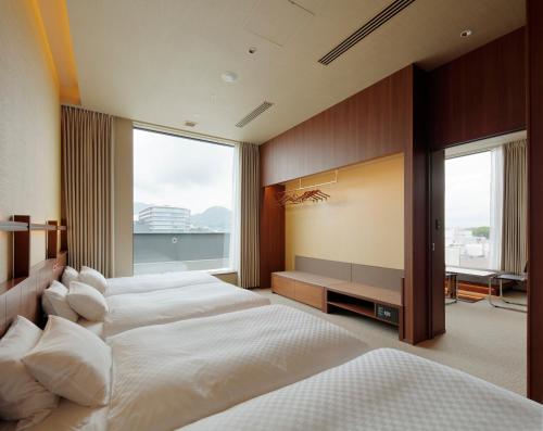 a bedroom with three beds and a large window at Candeo Hotels Kumamoto Shinshigai in Kumamoto