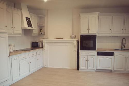 una cocina blanca con armarios blancos y electrodomésticos negros en Maison 3,5km de la plage et proche Mont St Michel en Saint-Broladre
