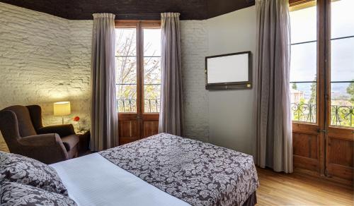 Schlafzimmer mit einem Bett, einem Stuhl und Fenstern in der Unterkunft Hotel Rural y Apartamentos Villa Engracia in L’Espluga de Francolí