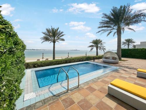 a swimming pool with palm trees and a beach at FAM Living - Sarai Beach Villas - Palm Jumeirah - Families Only in Dubai