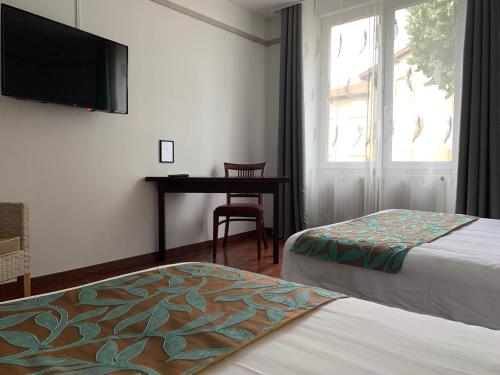 a hotel room with two beds and a desk and a television at L'EMBLEME - BOUTIQUE HOTEL in Beaurepaire