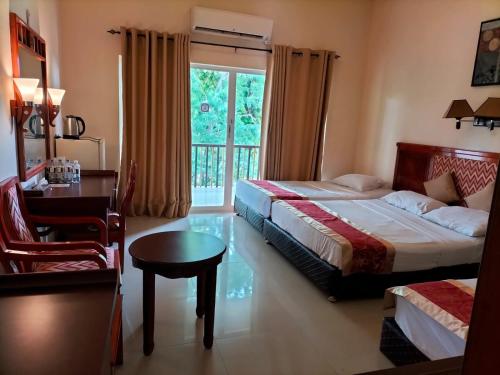 a bedroom with two beds and a desk and a window at Heritage Hotel in Anuradhapura