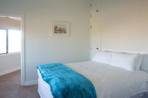 a bedroom with a white bed with a blue blanket on it at The Hydro Esplanade Apartments in Dunedin