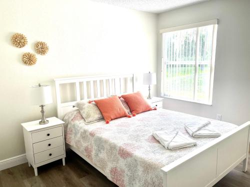 a white bedroom with a bed with orange pillows and a window at LOVELY RENOVATED APARTMENT 3/2 CLOSE DISNEY in Kissimmee