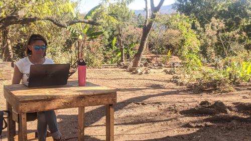 a woman sitting at a wooden table with a laptop at Hostal Tribu Malinalco in Malinalco