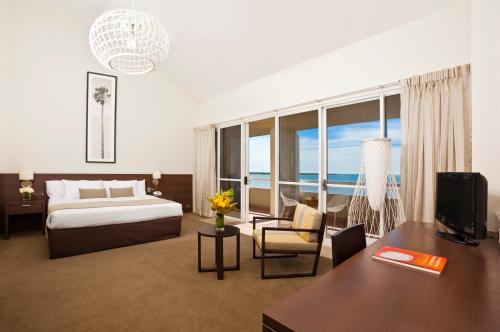 a hotel room with a bed and a desk with a television at Cairns Harbourside Hotel in Cairns