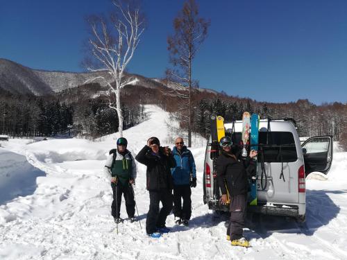 a group of people standing in the snow next to a van at Fujio Pension Madarao Apartment Hotel & Restaurant in Iiyama