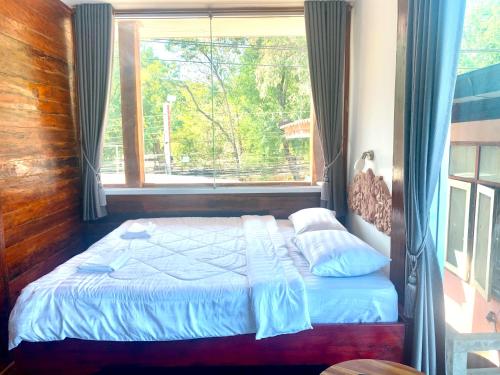 a bed in a room with a large window at Une Jai Place เรือนอุ่นใจ in Phimai