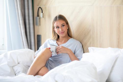 a woman sitting in bed holding a cup of coffee at T62 Hotel in Budapest