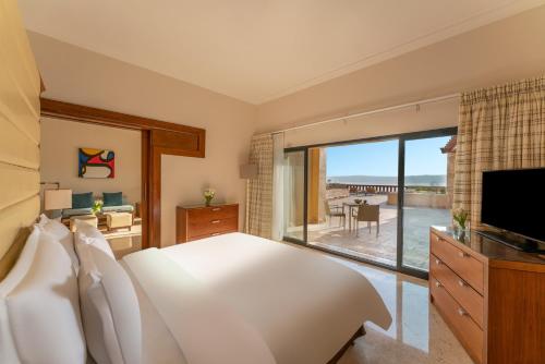 a bedroom with a large white bed and a large window at Mövenpick Resort & Spa Dead Sea in Sowayma
