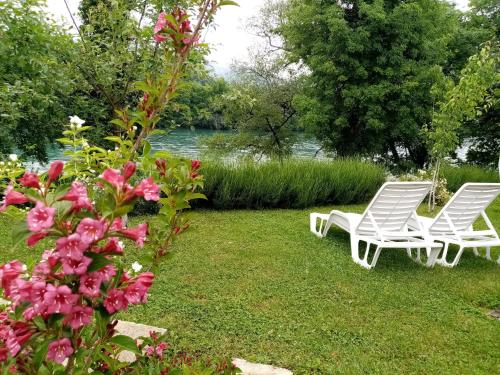 two white chairs sitting on the grass near a river at NIKOLIJA 3 in Bajina Bašta